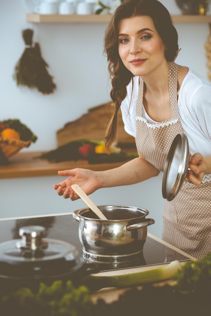 Joven morena cocinando sopa en la cocina. Ama de casa sosteniendo una cuchara de madera en la mano. Concepto de alimentación y salud.