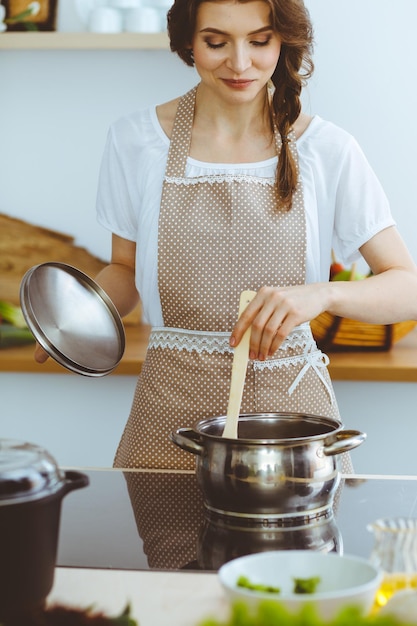 Joven morena cocinando sopa en la cocina. Ama de casa sosteniendo una cuchara de madera en la mano. Concepto de alimentación y salud.