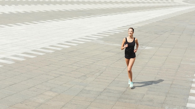 Joven morena corriendo en el centro de la ciudad, entrenando antes del maratón, copiando espacio