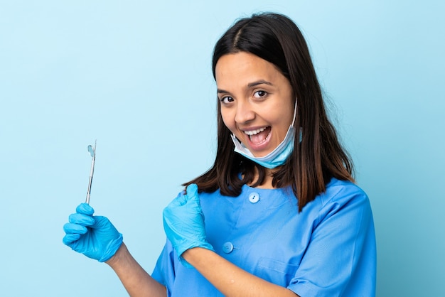 Joven morena dentista de raza mixta mujer sosteniendo herramientas sobre pared aislada celebrando una victoria