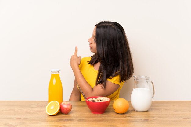 Joven morena desayunando leche apuntando hacia atrás con el dedo índice