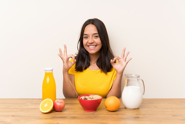 Joven morena desayunando leche mostrando un signo bien con los dedos