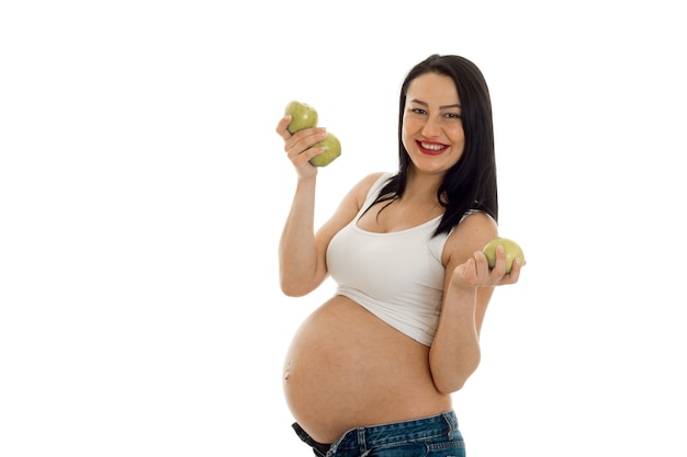 Joven morena embarazada posando con manzanas verdes aislado en la pared blanca