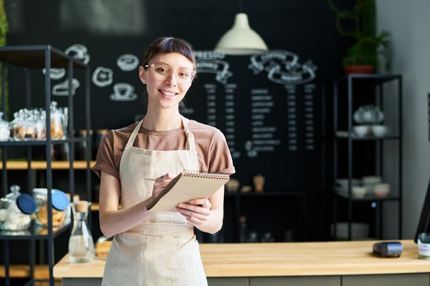 Joven morena empleada de cafetería haciendo notas en el bloc de notas