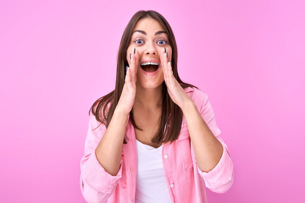 Foto joven morena feliz gritando y ahuecando las manos alrededor de la boca aislada sobre fondo rosa de estudio. ¡atención de noticias emocionada!