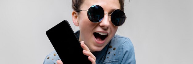 Joven morena en gafas redondas. Los pelos se recogen en un moño. Chica con un teléfono negro.