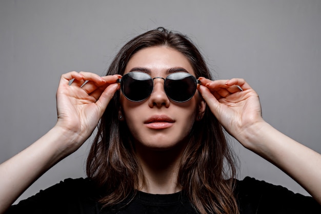 Joven morena con gafas de sol negras y una camiseta negra sobre gris