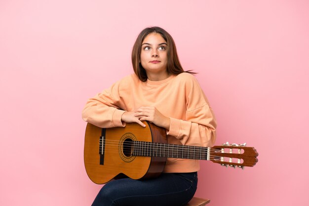 Joven morena con guitarra sobre rosa aislado haciendo dudas gesto mientras levanta los hombros