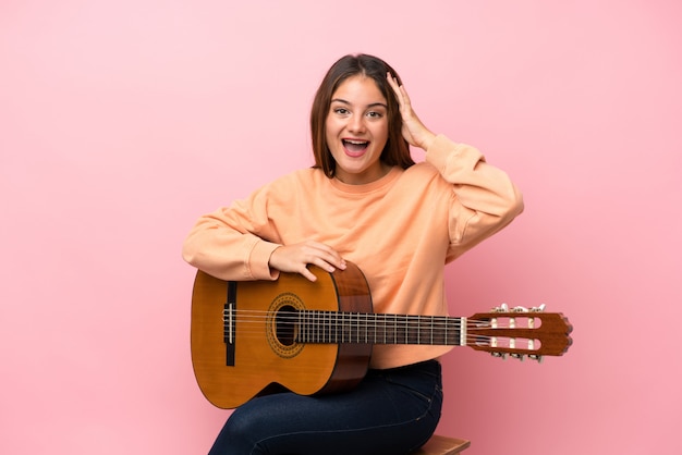 Joven morena con guitarra sobre rosa aislado con sorpresa y expresión facial conmocionada