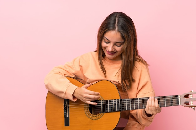 Joven morena con guitarra sobre rosa aislado