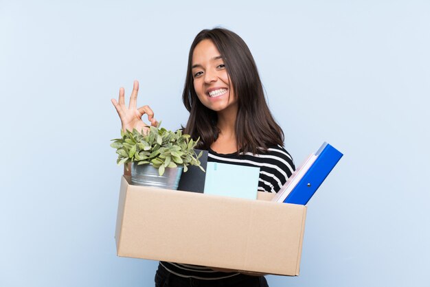 Joven morena haciendo un movimiento mientras recogía una caja llena de cosas que mostraban bien firmar con los dedos