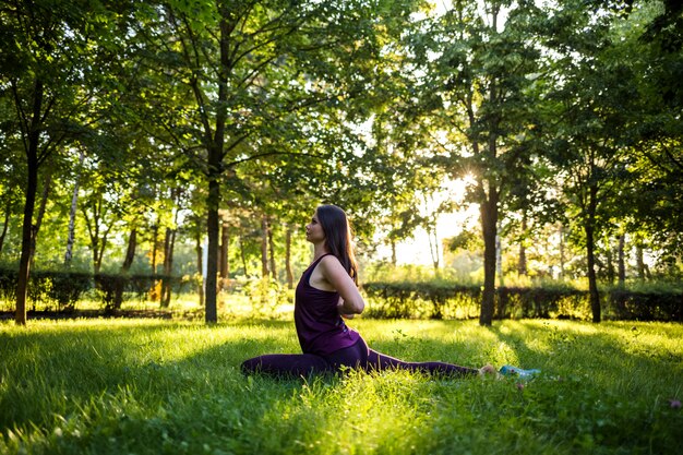 Joven morena haciendo yoga sobre una estera en el parque al atardecer