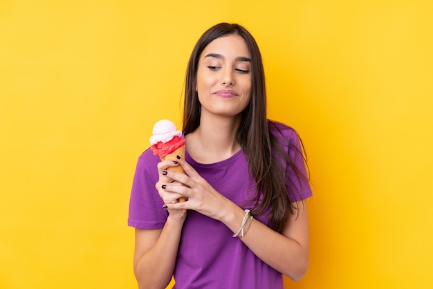 Joven morena con un helado de cucurucho sobre pared amarilla aislada