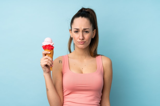 Joven morena con un helado de cucurucho sobre la pared azul aislada con expresión triste