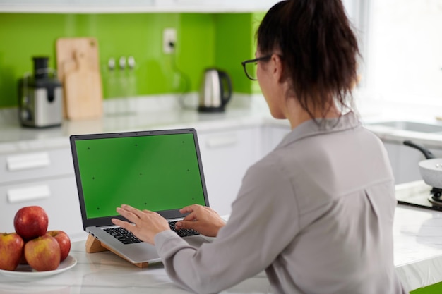 Joven morena independiente sentada frente a una laptop con pantalla verde