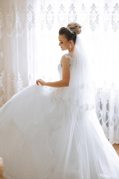 Foto una joven morena con un largo vestido de novia y un velo en la habitación del hotel una encantadora novia de tamaño completo en un magnífico vestido blanco la mañana antes de la boda