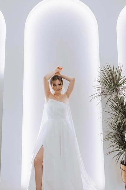 Joven morena en largo vestido de novia y velo en la habitación del hotel una encantadora novia de tamaño completo en un magnífico vestido blanco la mañana antes de la boda