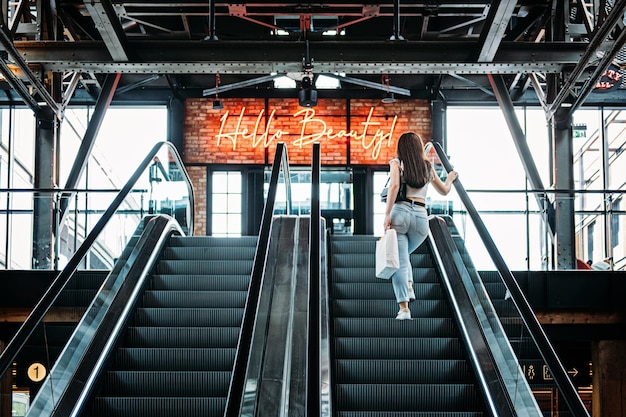 Joven morena latina atractiva mujer con bolsas de compras en escaleras mecánicas en el centro comercial de la tienda de moda