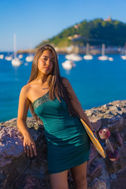 Una joven morena latina con un patín en un vestido verde con el mar de fondo