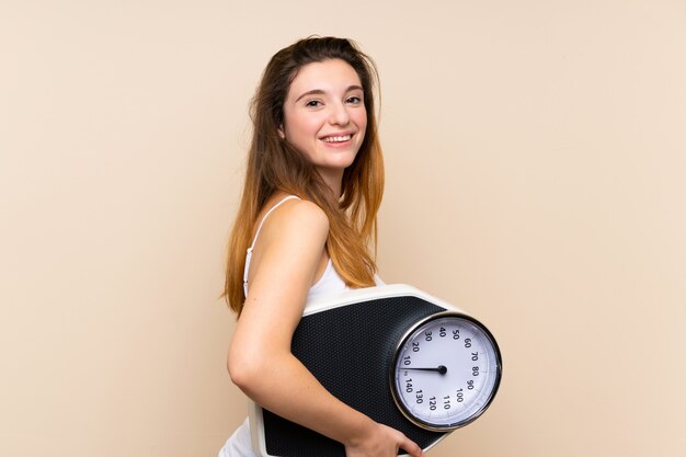 Joven morena con máquina de pesaje sobre pared aislada