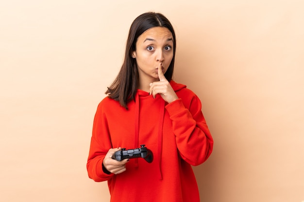 Foto joven morena mujer de raza mixta jugando con un controlador de videojuegos sobre aislados haciendo gesto de silencio