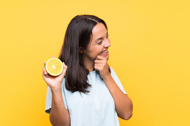 Joven morena con una naranja pensando en una idea y mirando de lado