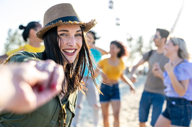 Joven morena con ojos azules invitándote a bailar en un festival internacional musical de fiesta en la playa con una gran multitud feliz de gente diversa