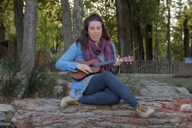 joven morena con el pelo largo tocando el ukelele en el campo sobre la hierba