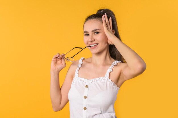 Joven morena con el pelo largo en un top blanco con gafas en los dientes sobre un fondo amarillo