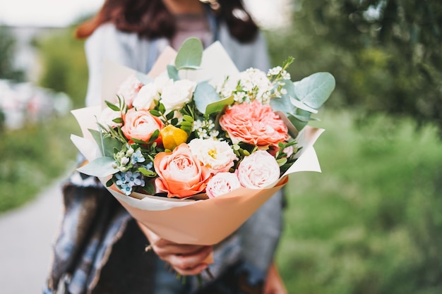 Joven morena con poncho y jeans sostiene un hermoso ramo de flores diferentes