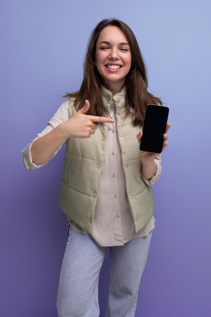 Joven morena positiva en estilo casual que muestra la pantalla del teléfono inteligente