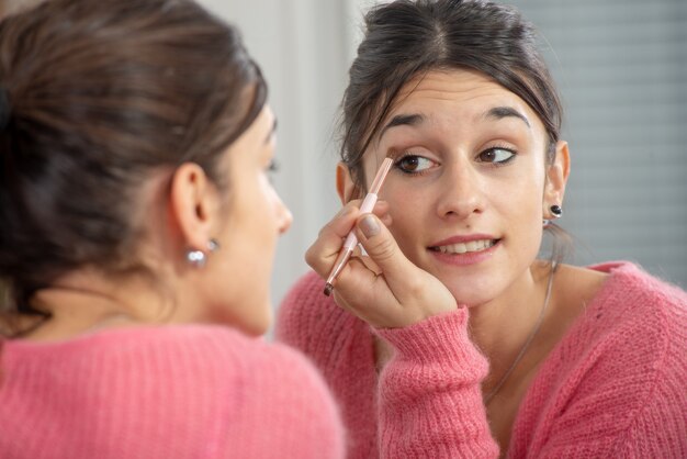 Una joven morena que pone maquillaje en el espejo