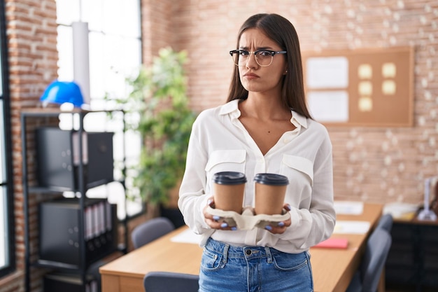 Joven morena que trabaja en la oficina sosteniendo café para llevar deprimida y preocupada por la angustia llorando enojada y asustada expresión triste