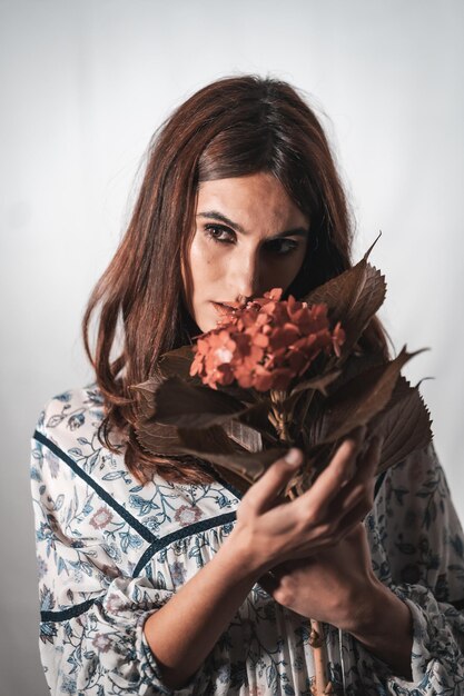 Una joven morena de raza caucásica con un vestido de flores vintage sobre un fondo blanco. Retrato con una flor roja en la mano, con una mirada dulce