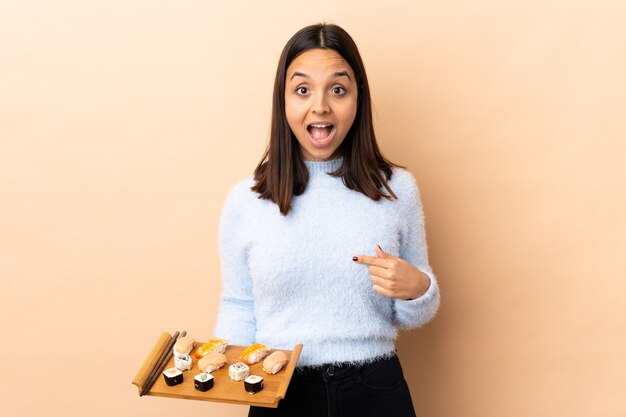 Foto joven morena de raza mixta mujer sosteniendo sushi aislado con expresión facial sorpresa