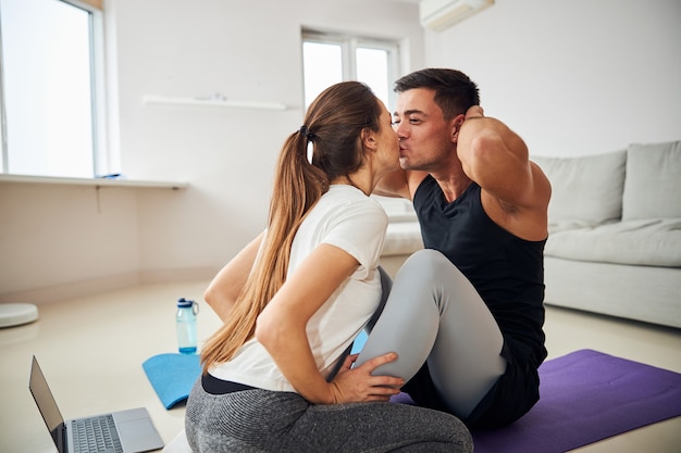 Joven morena recibiendo besos de su novia por hacer abdominales