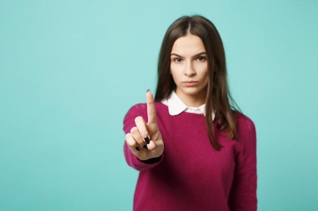 Una joven morena con ropa informal posando toca algo como pulsar un botón aislado en un retrato de estudio de fondo azul. Gente emociones sinceras concepto de estilo de vida. Simulacros de espacio de copia.