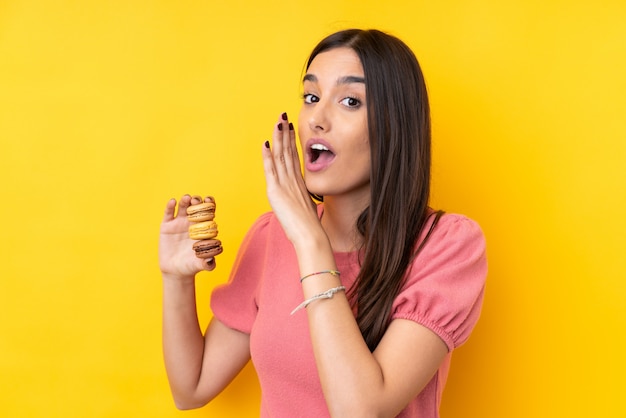 Joven morena sobre amarillo con coloridos macarons y susurrando algo