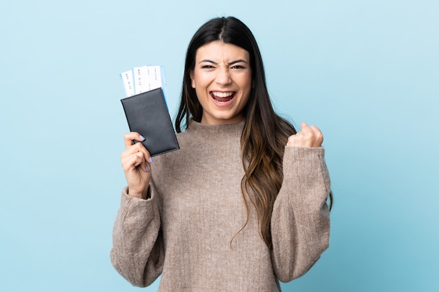 Joven morena sobre azul aislado feliz en vacaciones con pasaporte y boletos de avión