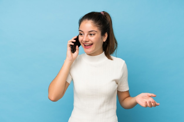 Joven morena sobre azul aislado manteniendo una conversación con el teléfono móvil con alguien