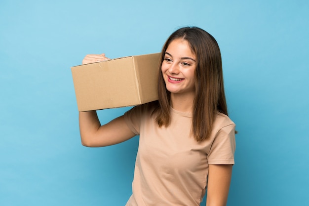 Foto joven morena sobre azul aislado sosteniendo una caja para moverlo a otro sitio