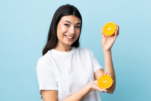 Joven morena sobre azul aislado sosteniendo una naranja