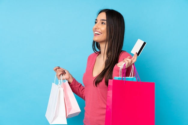 Foto joven morena sobre azul sosteniendo bolsas de compra y una tarjeta de crédito