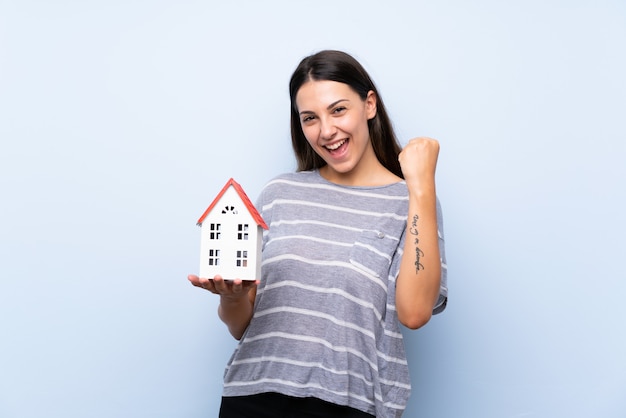 Foto joven morena sobre fondo azul aislado sosteniendo una casita