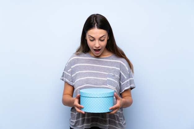 Joven morena sobre pared azul aislada con caja de regalo