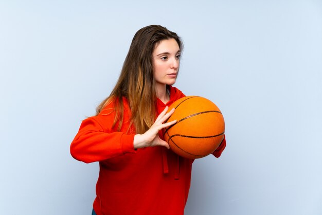 Joven morena sobre pared azul aislada con pelota de baloncesto