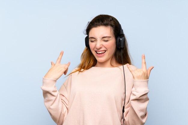 Joven morena sobre pared azul aislada usando el móvil con auriculares y baile