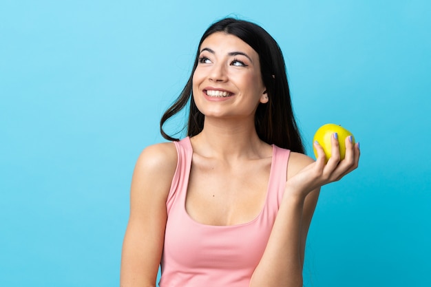 Joven morena sobre pared azul con una manzana y feliz