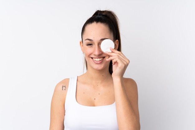 Foto joven morena sobre pared blanca aislada con algodón para quitar el maquillaje de la cara y sonriendo