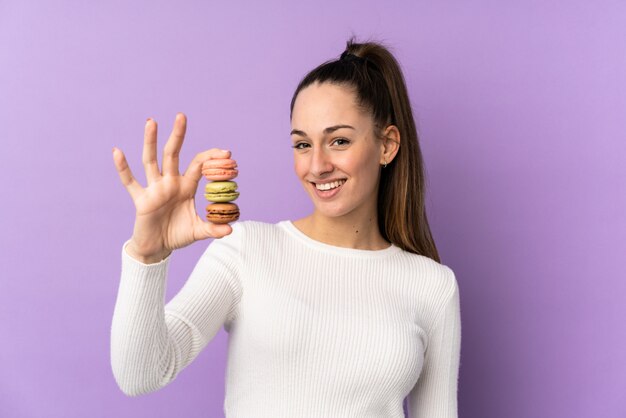 Foto joven morena sobre pared púrpura aislada con coloridos macarons franceses y con expresión feliz